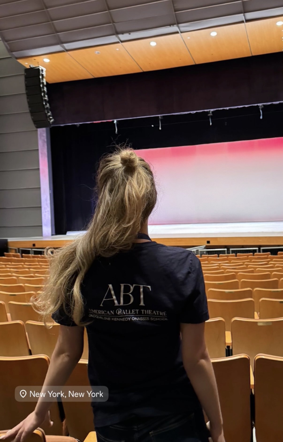 Teacher in an ABT Jacqueline Kennedy Onassis School shirt facing an empty theatre stage